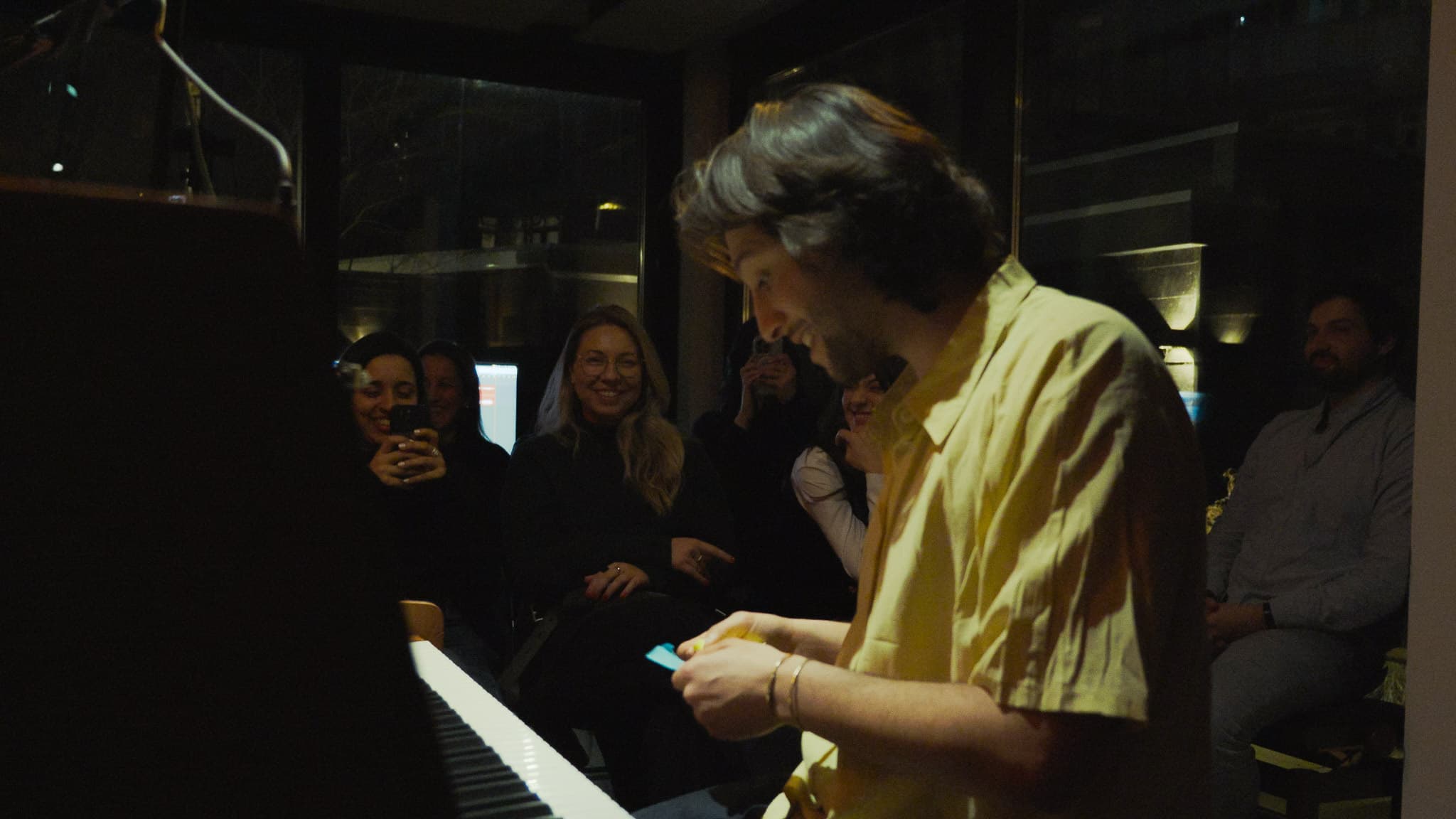 An evening in the Amsterdam studio: the artist at the opened upright piano, the audience close enough to lean in, warm light.