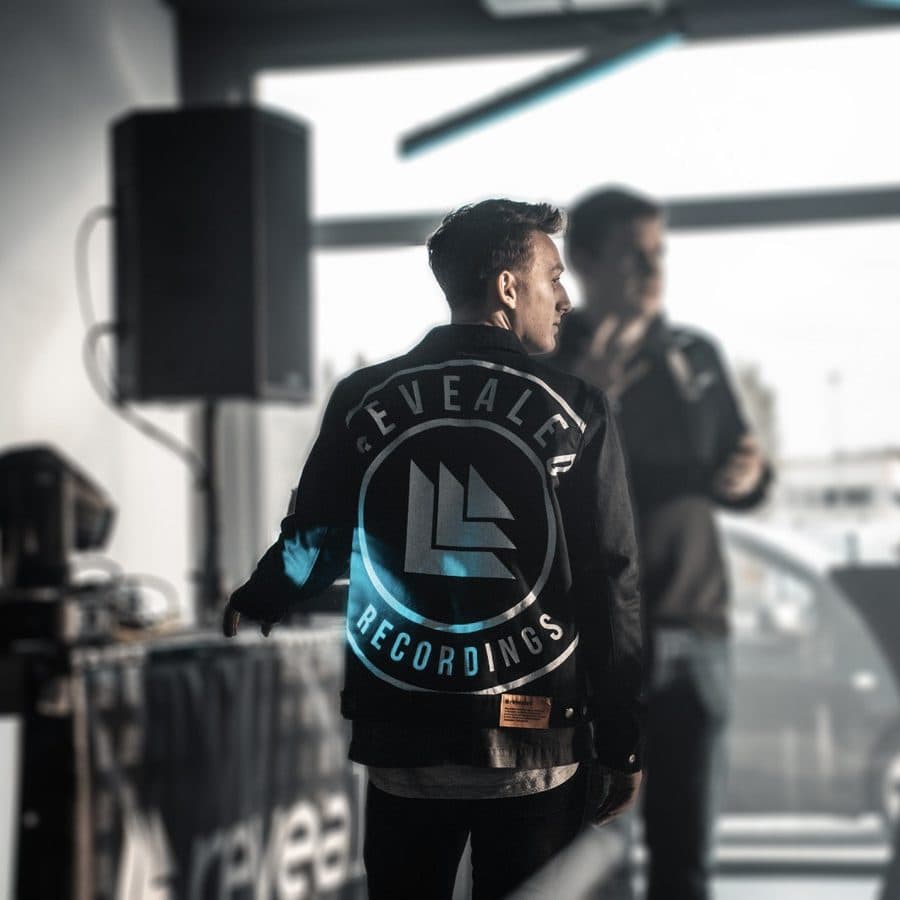 Ivo Adelaar in a Revealed Recordings crew jacket at a label event, seen from behind against the window light