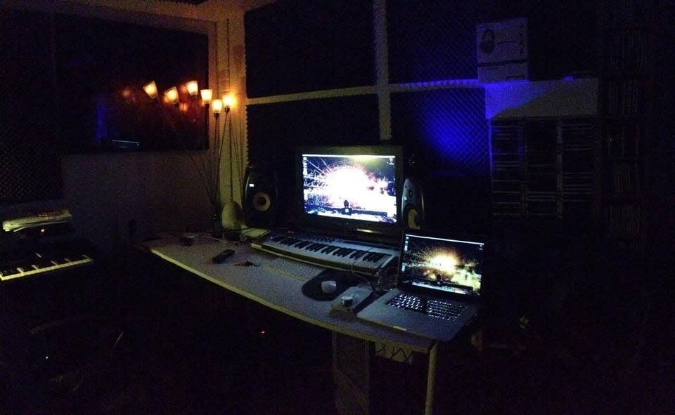 The first home studio in the garage at night: a monitor running a music program, a MIDI keyboard, studio monitors and racks of CDs